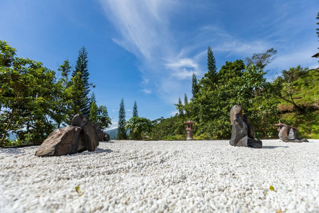 Peaceful Zen garden with stone sculptures set against a vibrant green backdrop and clear blue sky.