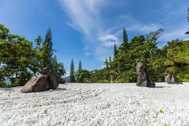 Peaceful Zen garden with stone sculptures set against a vibrant green backdrop and clear blue sky.